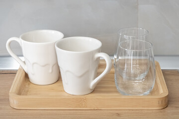 Two empty water glasses and two tea cups or mugs on a wooden tray in the kitchen, close up