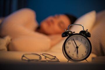 Woman is sleeping peacefully in her bedroom at night. Alarm clock in the foreground