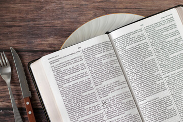 Open holy bible book in plate with fork and knife on wooden table. Top view. Spiritual food,...