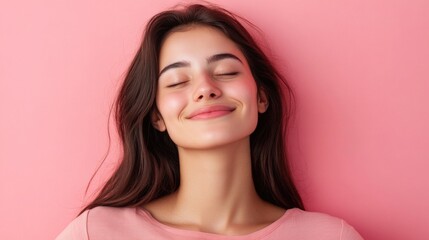 Brunette woman in light pink shirt smiles with eyes closed against a pastel pink background conveying relaxation and contentment