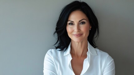 Obraz premium Confident woman with dark hair wearing a white shirt smiling against a gray background with copy space