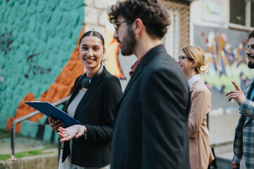 Group of business people enjoying a casual conversation while walking outside against a vibrant graffiti backdrop. The image captures teamwork, communication, and a modern urban setting.