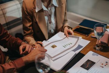 Business meeting with people analyzing reports and data on table. Collaborative discussion and analysis in cozy work environment. Papers and charts are the focus of the team's attention.
