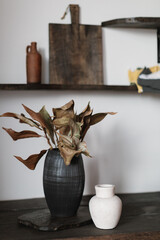 A stylish still life of decorative leaves arranged in a tall vase and a smaller white vase on a...