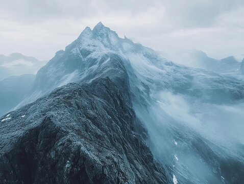 A majestic mountain peak shrouded in mist and snow reveals rocky ridges beneath a cloudy sky - Powered by Adobe
