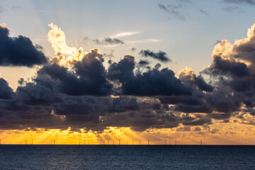 Evening sun behind dark clouds of a thunderstorm over silhouettes of wind turbines in the North sea