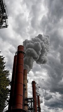 Vertical perspective, Industrial chimneys reaching into the clouds, Earthy tones with natural greens, Industrial and gritty
