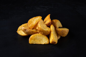 rustic baked potatoes neatly stacked in a pile on a stone cutting board on a black background. side angle view. fast food photography