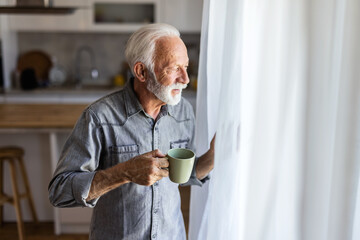 Senior man drinking coffee and looking thoughtfully out of a window. Old man feel happy drinking coffee in the morning, enjoying time in his home indoor background - lifestyle senior happiness concept