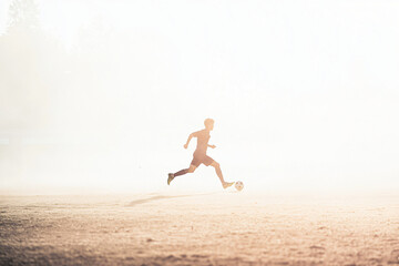 Obraz premium passionate youth soccer player running with ball through winter haze