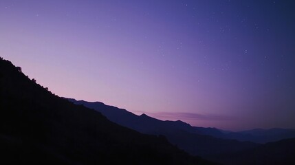 Fototapeta premium Mountain Silhouettes at Dusk: Soft purple hues and a starry sky above shadowed mountain peaks.