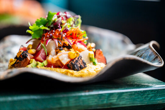 A colorful gourmet dish featuring grilled seafood atop a bed of vibrant vegetables and garnished with herbs and sauces. Served on an elegant, wavy plate, perfect for a culinary presentation.