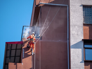 Worker on rope with safety gear performing industrial facade cleaning on tall building. Smoke, dust...