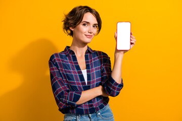 Photo of intelligent woman dressed checkered shirt presenting smartphone display web panel empty...