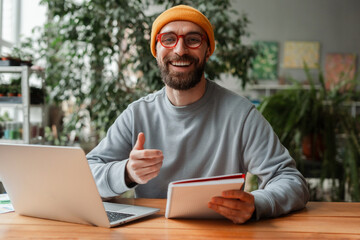 Happy entrepreneur showing thumbs up working from home office using laptop