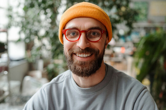 Portrait of smiling bearded man wearing glasses and yellow beanie looking at camera