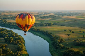 Fototapeta premium Colorful hot air balloon floating serenely over a picturesque landscape of green fields and a winding river at sunset