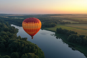 Colorful hot air balloon flying over beautiful landscape with river and forest at sunset