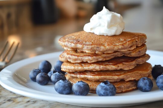 A stack of whole grain pancakes with fresh blueberries and a dollop of whipped cream