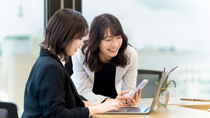 パソコンとスマホを使いながら話す2人の女性・ビジネスウーマン