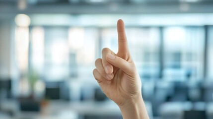 Male hand making OK gesture with raised index finger against blurred modern office background featuring soft blue and gray tones
