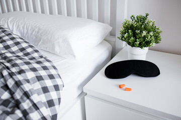 Cozy bedroom setup with sleep mask, earplugs, and plant on white nightstand