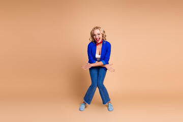 Joyful woman posing stylishly in blue jacket and scarf on beige background