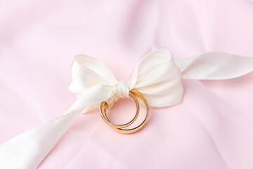 Wedding rings tied with ribbon on pink cloth, closeup