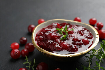 Tasty cranberry sauce in bowl, berries and thyme on black table, closeup