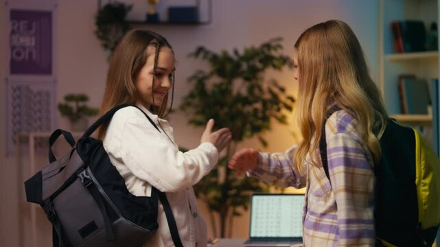 Two teen girls greet each other in class, giving a high five and bumping fists