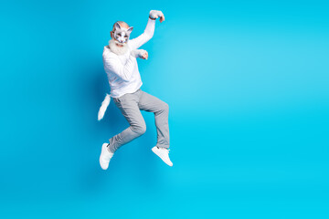 Obraz premium Elderly man in a fun outfit with cat mask jumping joyfully against a blue background