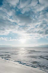 Bright sun shining over over the frozen sea. Winter seascape: clouds above the huge lake covered with ice and snow.