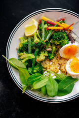 Healthy vegetable grain bowl with broccoli, green beans, baby spinach, soft-boiled egg, lemon wedge, and colorful carrots. Nutritious lunch with vibrant ingredients