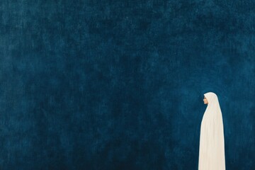 A serene portrait of a Muslim woman in a white hijab standing against a deep blue textured background, embodying tranquility and grace, highlighting cultural identity and modesty