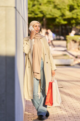 Muslim woman using smartphone and holding shopping bags