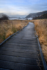 Obraz premium Wooden footpath leading through countryside with mountains in background. Borrowdale, Keswick, Lake District, UK.