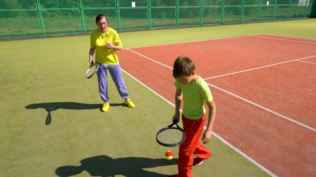 Boy and woman tennis coach hitting balls with tennis racket on court