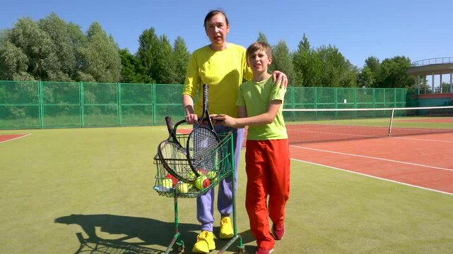 A mother coach and a teenage boy are walking on a tennis court and talking.
