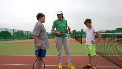 On the tennis court, a female coach trains teenagers to play lawn tennis.