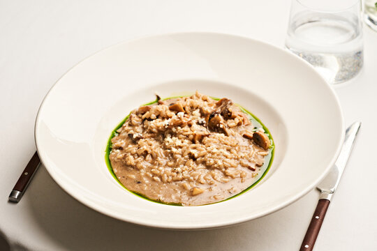 A creamy risotto is presented in a wide, white bowl, garnished with herbs and possibly cheese