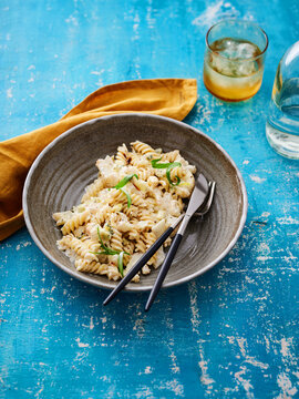 Creamy fusilli pasta. A beautiful bowl of creamy pasta topped with fresh basil sits on a textured blue surface, accompanied by a glass of beverage and a yellow napkin