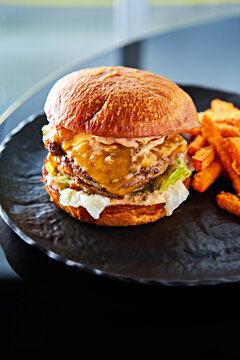 A delicious cheeseburger layers grilled meat, melted cheese, and fresh vegetables in a toasted bun, paired with crispy sweet potato fries on the side