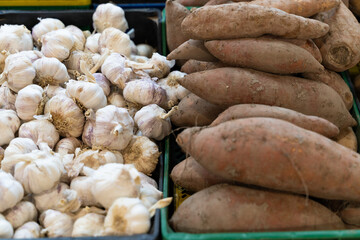white garlic and sweet potatoes on a stand at a farmers market