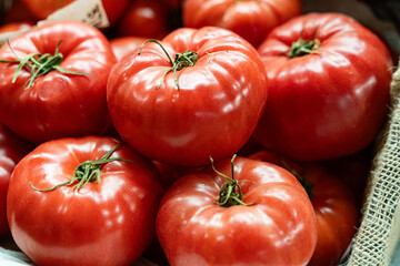 large, bright red tomatoes stacked on a rustic stall at a farmers' market, symbolizing freshness,...