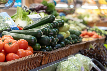 Fresh tomatoes, green and white zucchinis, cabbage, and leafy lettuce are beautifully arranged in woven baskets on a farmer's market stall, showcasing healthy, organic produce