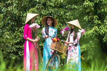 Young pretty Vietnamese women in traditional Ao Dai clothing with vietnam hat in green park