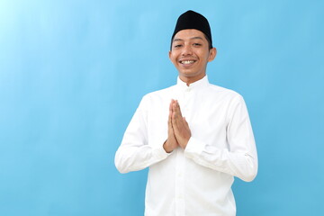 Asian Muslim man smiling to give greeting during Ramadan and Eid Al Fitr celebration blue background