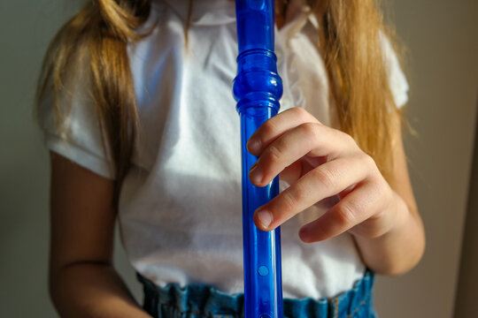 Little girl playing with skill the soprano recorder, blue flute. Close up - Powered by Adobe