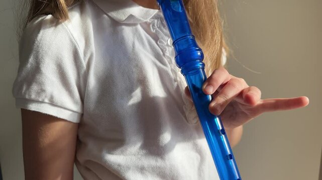 Little girl plays the blue flute. Close-up