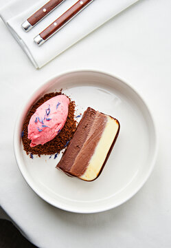 A tempting dessert features layers of chocolate cake alongside a scoop of pink berry sorbet. The dish is presented elegantly on a white plate, showcasing its vibrant colors